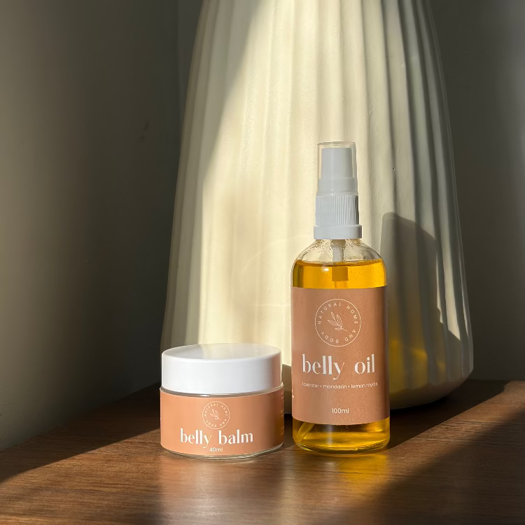 Belly oil and balm with a decorative vase in the background on a wooden surface.