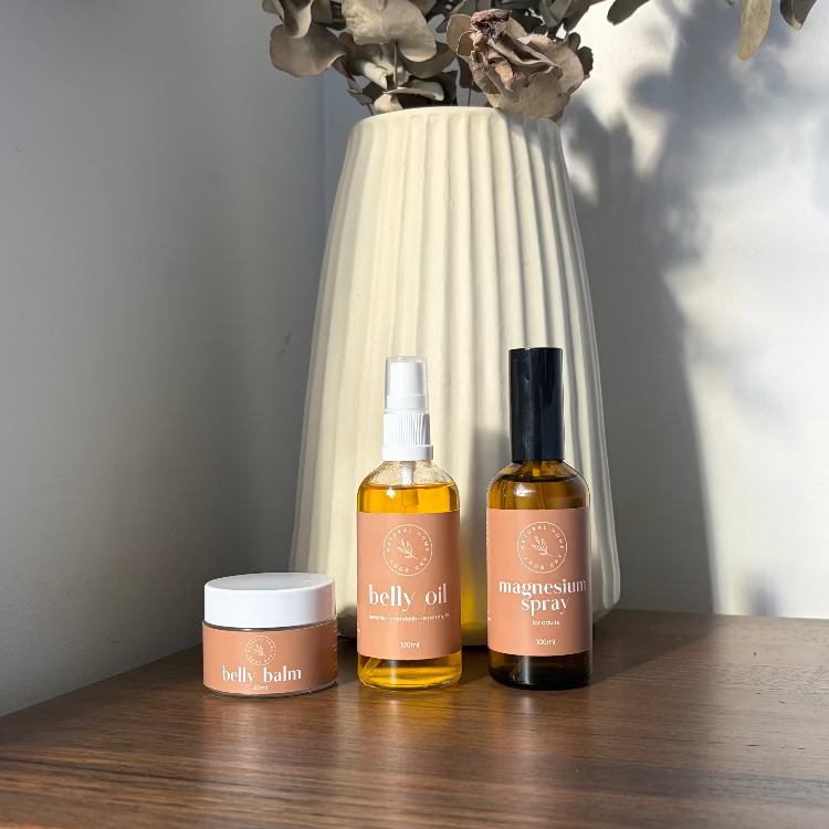 Three skincare products on a wooden surface with a vase and eucalyptus branches in the background.