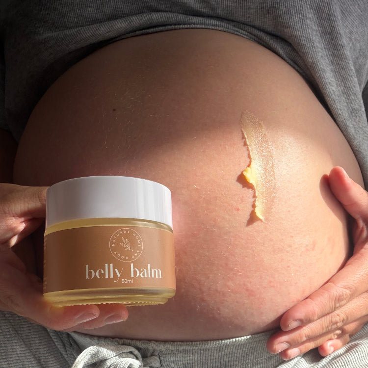 Person holding a jar of 'belly balm' against a pregnant belly with a visible stretch mark.